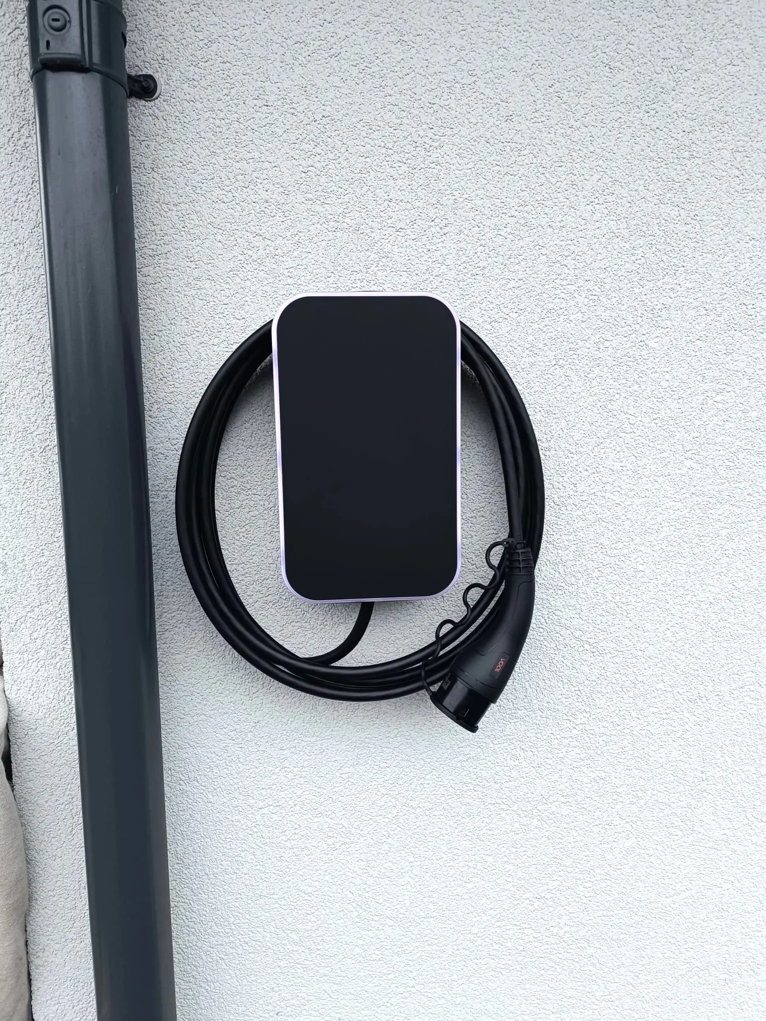 Svart elbillader med kabel på en hvit vegg